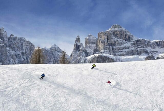 Skiers on a wide piste below the Dolomite walls in Alta Badia
