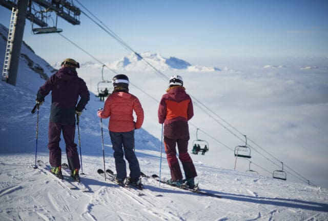 Three skiers beside a chairlift looking out over a sea of cloud