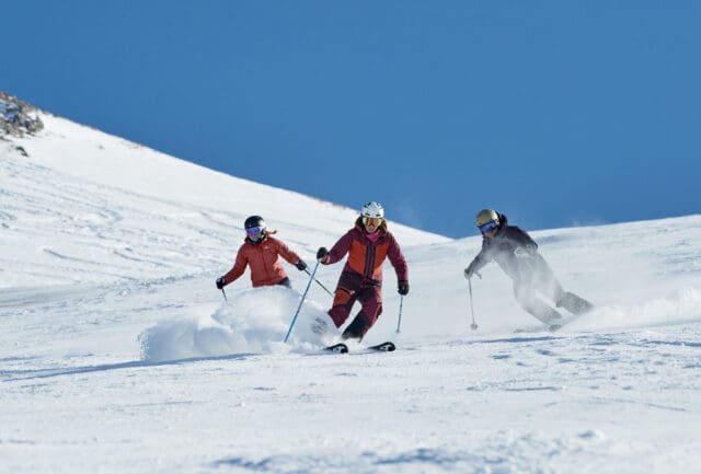 Three skiers making turns down a sunny piste