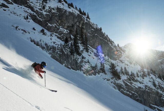 Skier turning through steep powder below rocky slopes