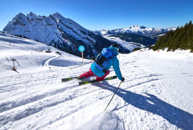 Skier carving a groomed piste with a rocky peak and ski lift behind