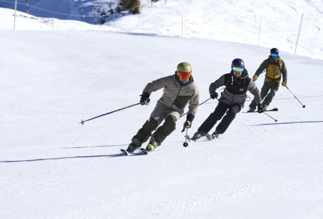 Three skiers following each other down a groomed piste