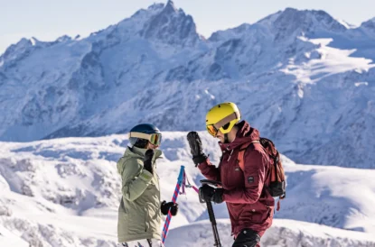 a high five between a pair of skiers, the blurry background of enormous, snow covered mountains sits impressively behind them