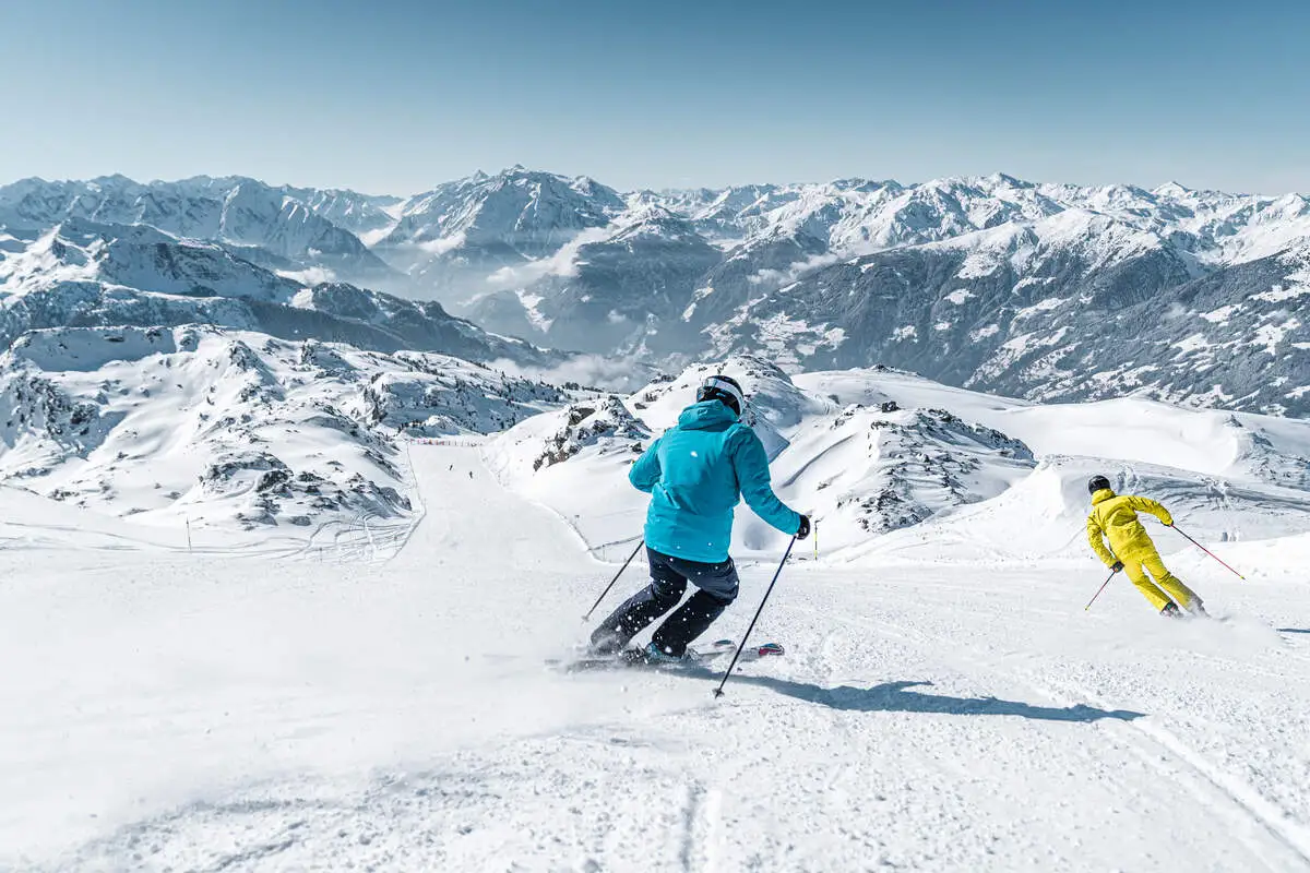 a skier on corduroy piste skiing on a blue run with a huge valley-mountain vista ahead