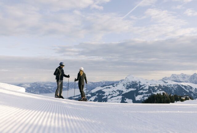 two skiers standing on perfect groomed piste looking out over a view