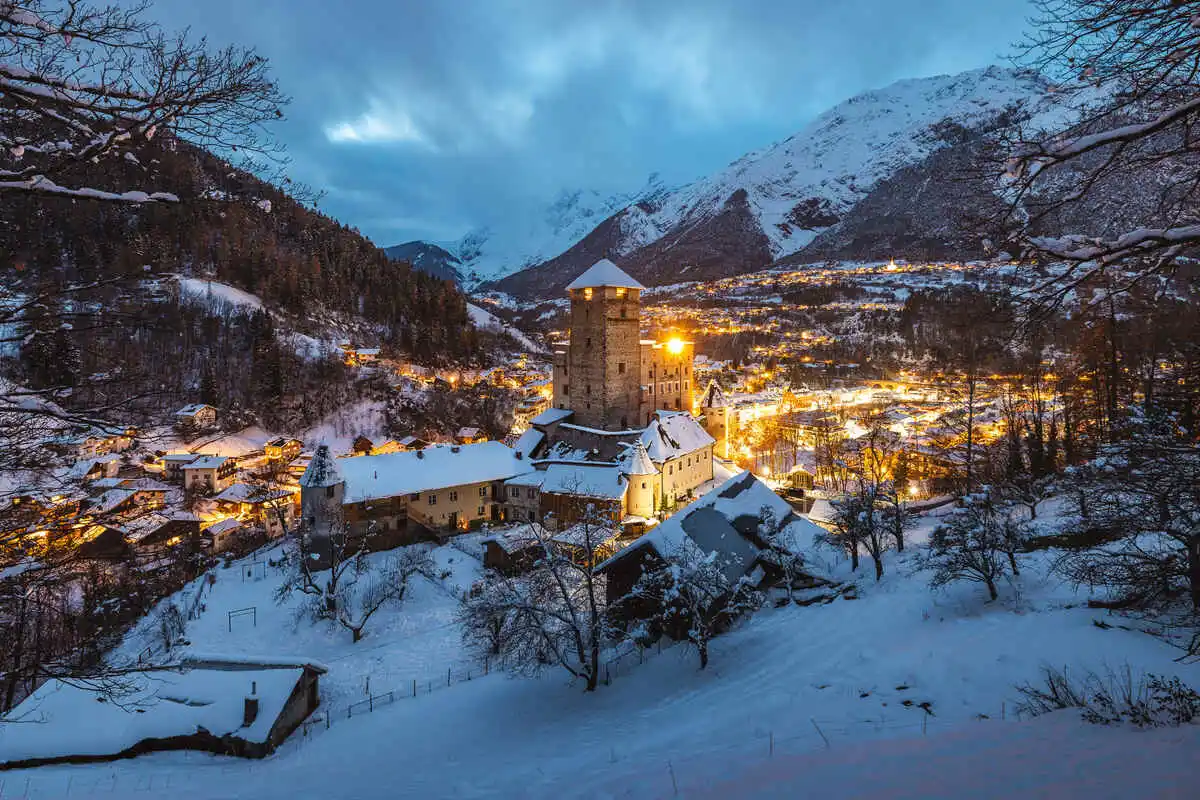 a lit up alpine village at dusk, covered in snow
