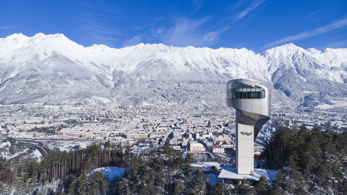 ski jump silver building in the foreground against the snow covered city of innsbruck behind