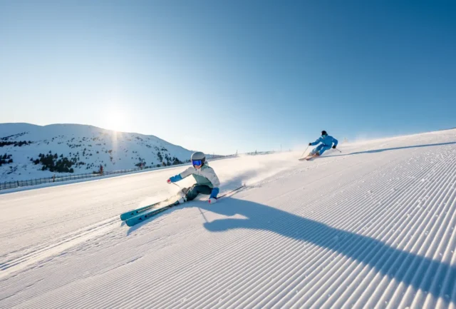 Two skiers carving fast turns on freshly groomed pistes at Hochkönig, Austria, with sunrise over the snow-covered peaks