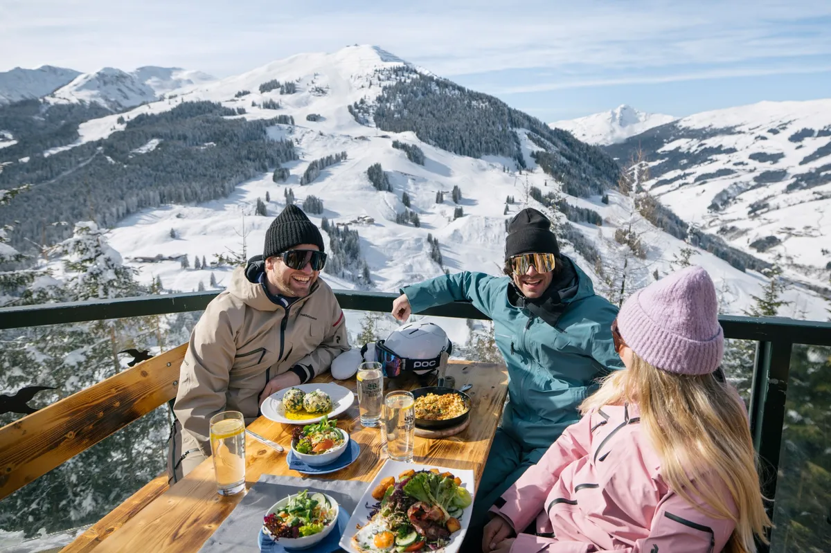 Friends enjoying food on a sun terrace overlooking snowy ski slopes