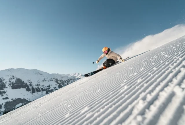 Skier carving on a groomed piste with Saalbach Hinterglemm peaks in the background