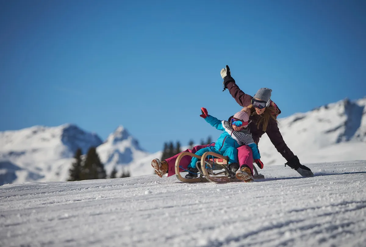 Parent and child sledding on a snowy slope in Saalbach Hinterglemm