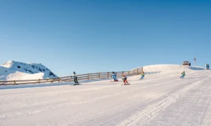 Group of skiers descending a broad piste under clear blue skies in Hochkönig ski region