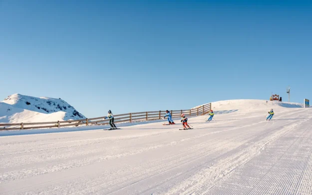 Group of skiers descending a broad piste under clear blue skies in Hochkönig ski region