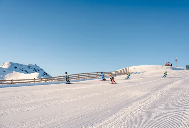 Group of skiers descending a broad piste under clear blue skies in Hochkönig ski region