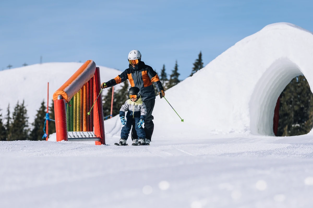 a father and child ski through a kids ski zone with fun elements