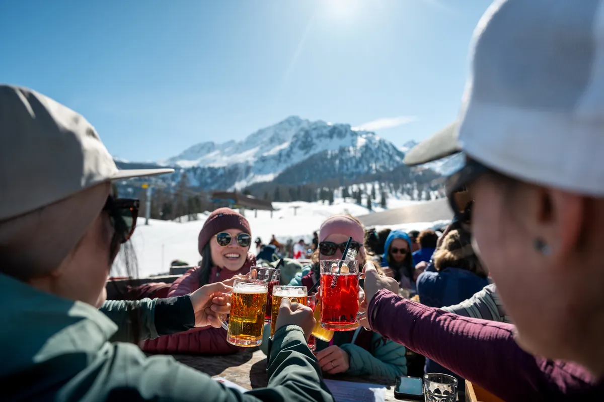 a group of friends cheers with full glasses outside on a sunny terrace in the snowy mountains
