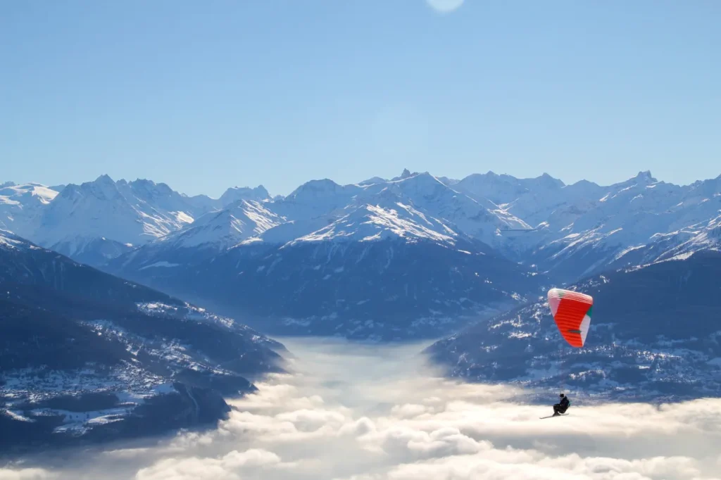 Paraglider flying above a sea of clouds with snow-covered Swiss Alps in the distance