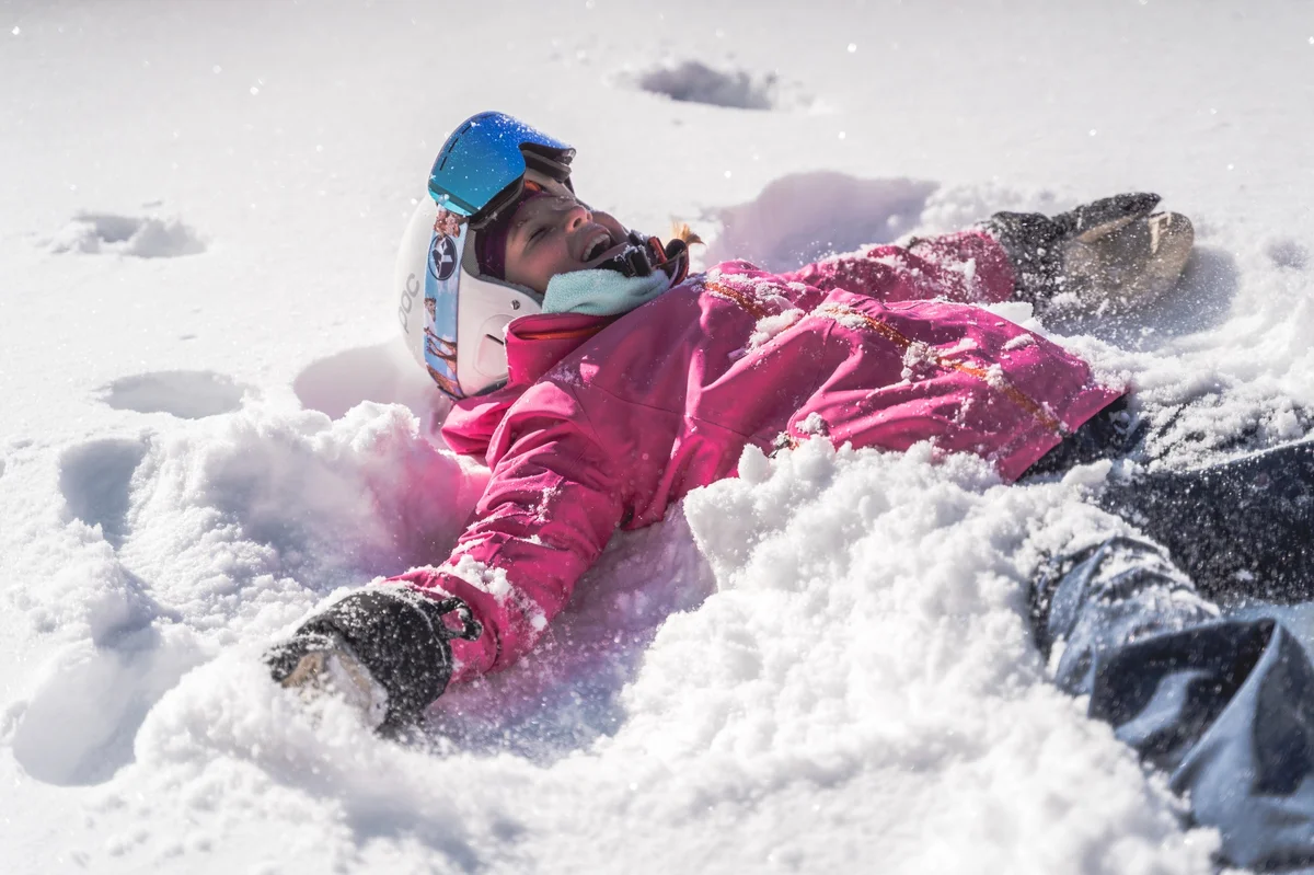 a girl in pink lying in fresh snow making a snow angel