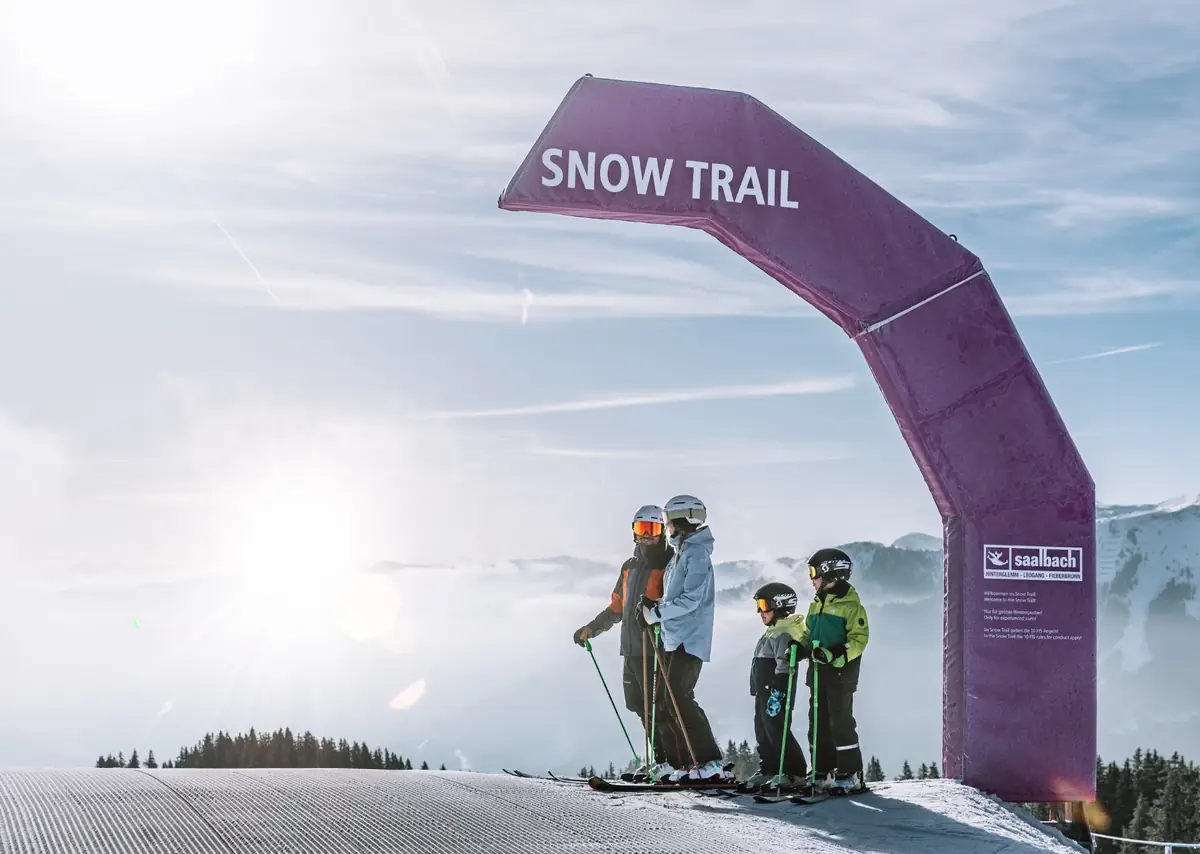 Family skiing together on a groomed slope in Saalbach, with panoramic alpine peaks behind them on a clear winter day.