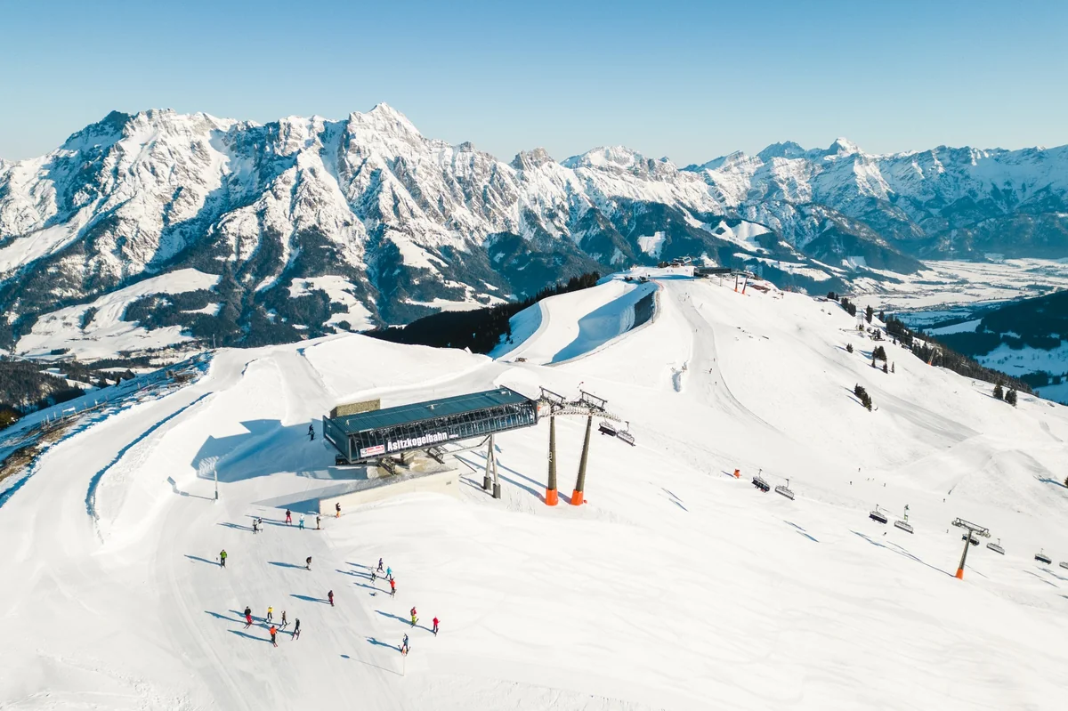 Panoramic view of the Asitz ski area in Saalbach, with groomed slopes, chairlifts, and snow-covered alpine peaks under a clear blue sky.