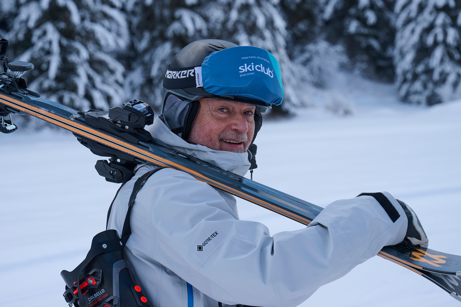 Smiling Peak Experience member carrying his skis through snowy woods