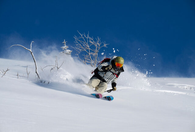 Skier bursting through deep powder under a clear blue sky