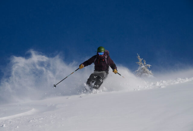 Skier throwing up powder under a deep blue sky