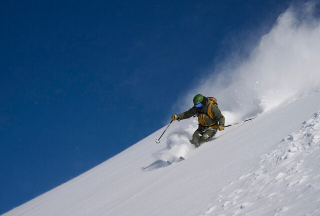 Skier turning down a steep powder slope under a deep blue sky