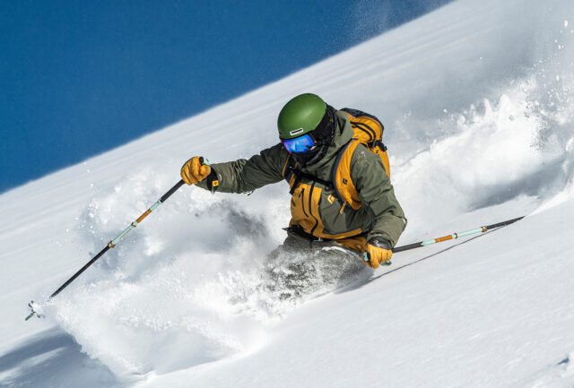 Skier in a green helmet throwing up powder on a steep off-piste slope