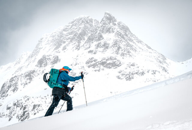 Ski tourer climbing a snowy slope below a rocky peak
