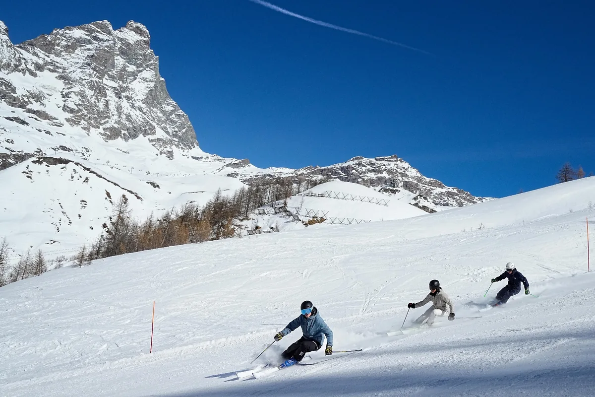 three skiers follow each other down the piste in a carving arc