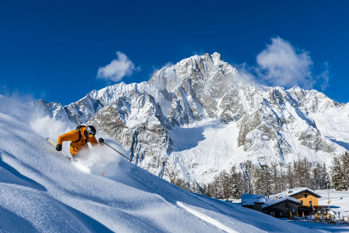 Skier carving through powder in Courmayeur with the snow-covered Mont Blanc massif rising behind.