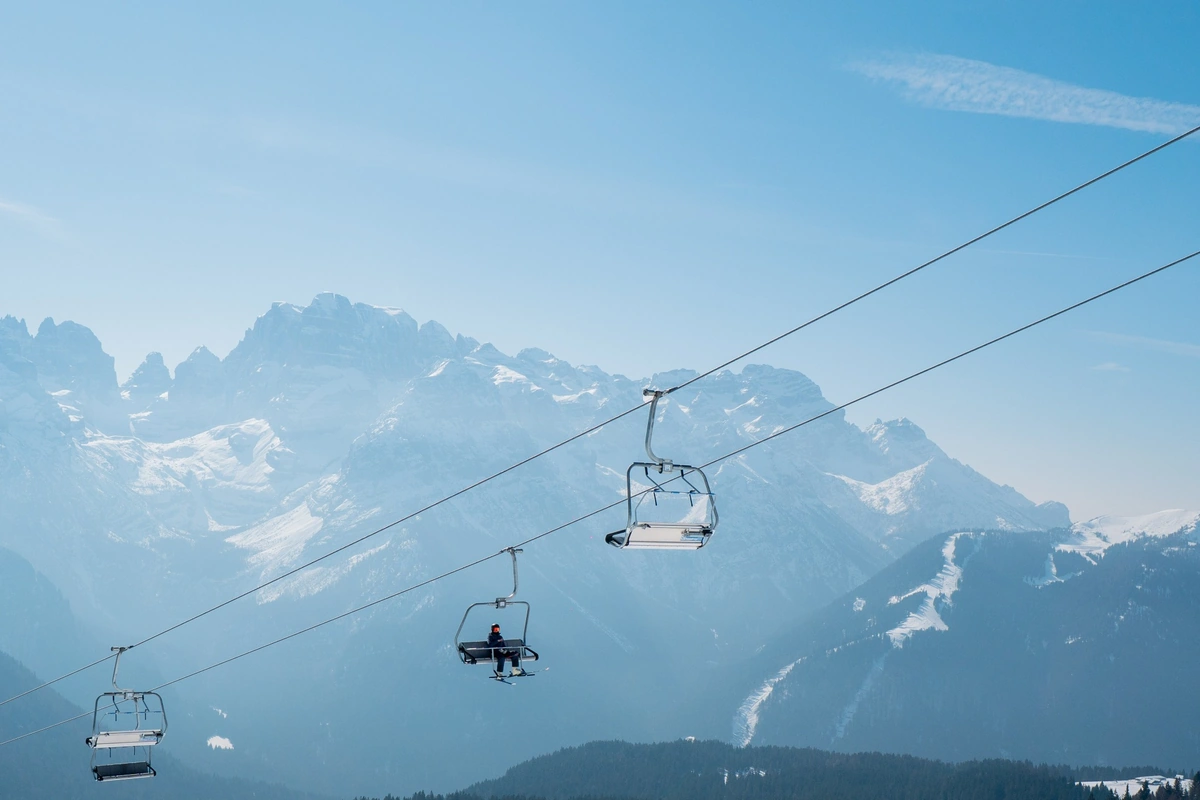Chairlift rising above the ski slopes with the snow-covered Dolomites in the distance.