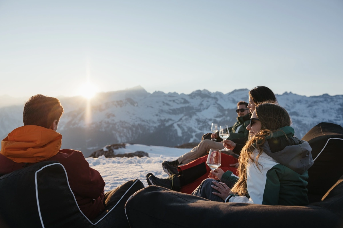 friends relaxing with drinks at sunset overlooking the snow-covered Dolomites.