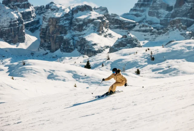 skier in yellow mid-turn on a piste, rocky dolomite mountain tops behind