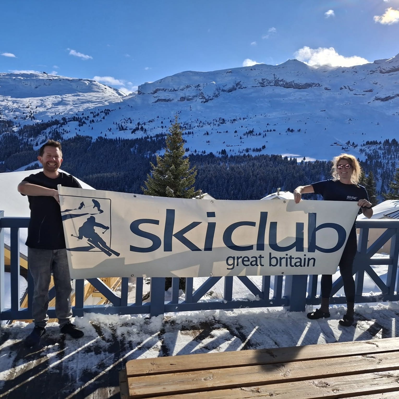 Pete and Rachel, chalet hosts in Flaine, holding a Ski Club banner on the chalet balcony