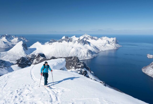 Ski tourer climbing a snowy ridge above a Norwegian fjord
