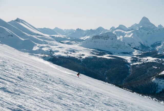 Skier on a wide groomed run with the Canadian Rockies behind