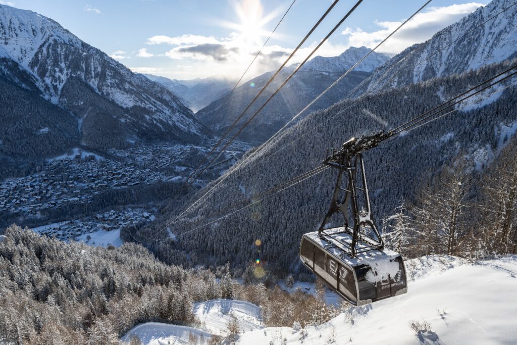 Cable car above snow-covered forest, with Courmayeur village in the valley below
