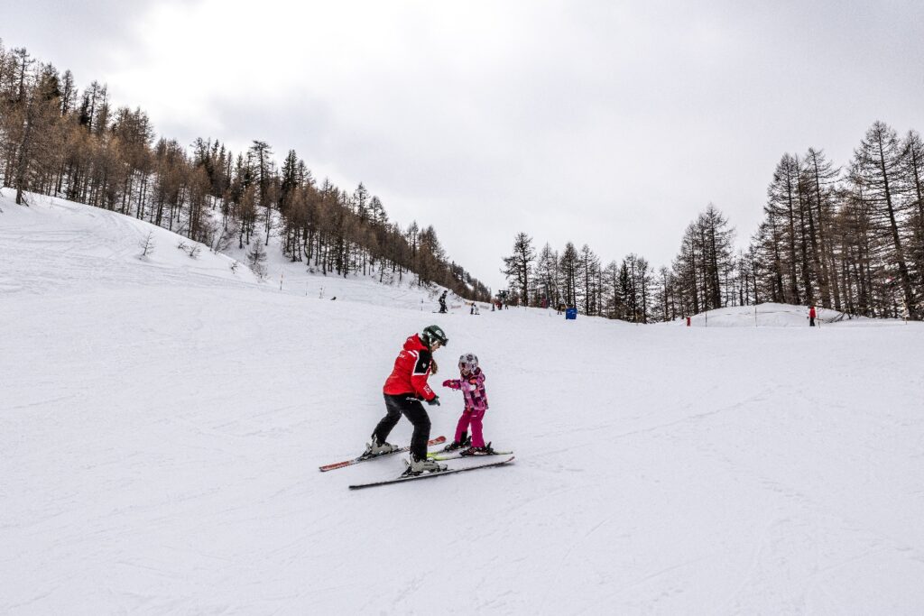 Ski instructor teaching a young child on a gentle tree-lined piste in Courmayeur