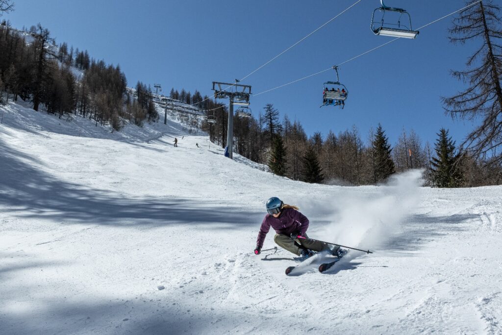 Skier carving on a sunny piste beside a chairlift in Courmayeur