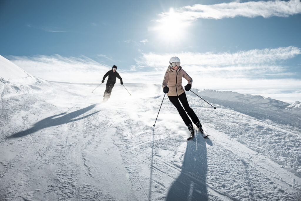 Two skiers carving down a wide, sunlit piste in Gurgl