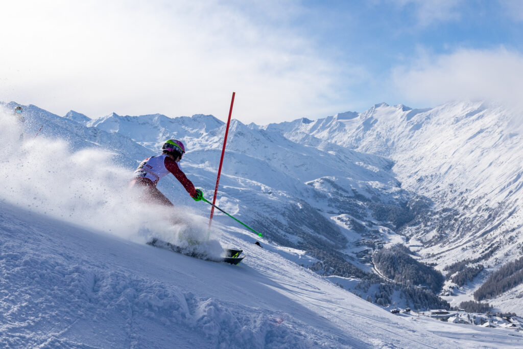A slalom racer rounds a red gate on the World Cup course in Hochgurgl, with the valley and peaks behind